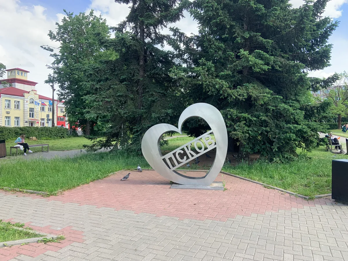 Металлический арт-объект в форме сердца с надписью «Псков» в Сквере Искусств летом — туристы фотографируются у скульптуры