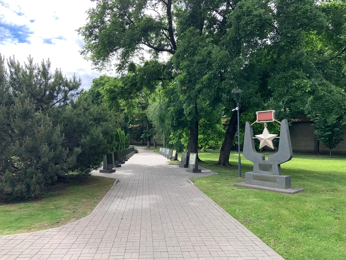 Аллея Героев в Пскове летом — широкая плиточная дорожка, гранитные стелы с именами Героев, справа памятник со звездой